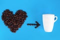 Heart shape made from coffee beans with white cup of coffee on blue background. World coffee day. Close-up. Top view Royalty Free Stock Photo