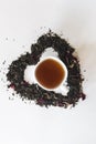 Heart shape made with a mixture of a variety of dried tea leaves and a cup of black tea Royalty Free Stock Photo