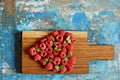 Heart shape made of premium raspberries on a wooden board on a blue background. Close up, top view. Romantic concept.