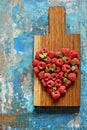 Heart shape made of premium raspberries on a wooden board on a blue background. Close up, top view. Romantic concept.