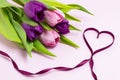 Heart shape made of purple ribbon and bouquet of purple and pink tulips on a light pink background.