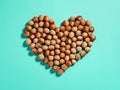 Heart shape made of unpeeled hazelnuts casts shadows on a turquoise paper background. Nuts as an antioxidant and protein source