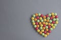 Heart shape from multi-colored tablets of dragees on a gray woven background
