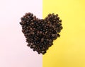 Heart shape roasted coffee beans brown and dark seed variation on half pastel pink and yellow background Royalty Free Stock Photo
