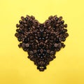 Heart shape roasted coffee beans brown and dark seed variation on yellow background Royalty Free Stock Photo