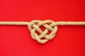 Heart shape rope knot on red background. Jute rope celtic knot.