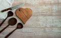 Heart-shaped beech cutting board, linen tablecloth napkin, large wooden spoons and a chef`s knife on a light wooden background. Royalty Free Stock Photo