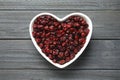 Heart shaped bowl with cranberries on wooden background, top view. Dried fruit