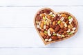 Heart shaped bowl with mixed nuts on white wooden table top view. Healthy food and snack Royalty Free Stock Photo