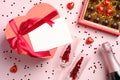 Heart-shaped box with blank paper card, box of chocolates, bottle of champagne and glasses with confetti on pink background. Royalty Free Stock Photo