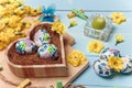 Heart shaped box with decorated Easter eggs, yellow flowers, burning candle and brown boards on wooden blue background. Spring Royalty Free Stock Photo