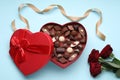 Heart shaped box with delicious chocolate candies, roses and ribbon on light blue background, flat lay Royalty Free Stock Photo