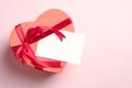 Heart shaped box with red ribbon bow and blank paper card on pink background. Flat lay, top view. Valentine`s day, Mother`s day, Royalty Free Stock Photo