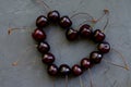 Heart shaped cherries with stalks close up as concept of berries loving. Grey old stone dark backdrop