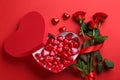 Heart shaped chocolate candies and bouquet on red background, flat lay Royalty Free Stock Photo