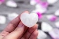 Heart-shaped clear quartz crystal in a female hand, pink rose petals background, healing Royalty Free Stock Photo