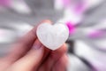 Heart-shaped clear quartz crystal in a female hand, pink rose petals background, healing, radial blur Royalty Free Stock Photo