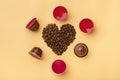 Heart shaped coffee beans and capsules around on beige background