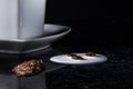 A heart shaped coffee cup with coffee beans, spilled milk and brown sugar on a black background with silver lining.