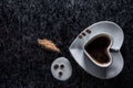 A heart shaped coffee cup with coffee beans, spilled milk and brown sugar on a black background with silver lining