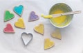 Heart shaped colorful iced cookies being iced on white baking paper background, top view Royalty Free Stock Photo