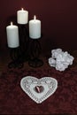Heart shaped dollie and gemstone, three white candles in metal holders and bouquet of white roses on wooden table.