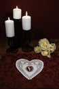 Heart shaped dollie and gemstone, three white candles in metal holders and bouquet of yellow roses on wooden table.