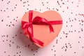 Heart shaped gift box with red ribbon bow and confetti on pink desk. Happy Valentines day, Mothers day, birthday concept. Flat lay Royalty Free Stock Photo