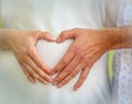 Hands of a man and a woman joined together in a heart shape over the belly of a pregnant woman Royalty Free Stock Photo