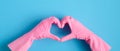 Heart shaped hands in pink rubber gloves over blue background. House cleaning service and housekeeping concept