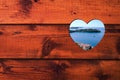 Heart shaped hole with blue sea, green island and coastal town in a brown wooden wall. Royalty Free Stock Photo