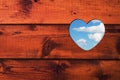 Heart shaped hole with blue sky and white clouds in a brown wooden wall. Royalty Free Stock Photo