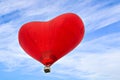 Heart-shaped hot air balloon flying over a blue sky with white clouds Royalty Free Stock Photo