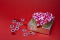 Heart shaped metal box filled with pink and white coated candy sitting on a gold present box