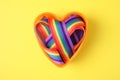 Heart shaped mold with bright rainbow ribbon on color background. Symbol of gay community