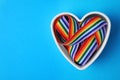 Heart shaped mold and bright rainbow ribbon on color background, top view. Symbol of gay community