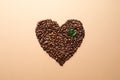 Heart shaped pile of coffee beans and fresh green leaves on light orange background Royalty Free Stock Photo