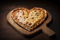 a heart-shaped pizza with melted cheese and a steamy crust, resting on a wooden board.