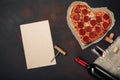 Heart shaped pizza with mozzarella, sausagered with a bottle of wine and wineglas, paper. Valentines day greeting card on rusty ba Royalty Free Stock Photo