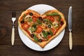 Heart shaped pizza on white plate with fork and knife ready to eat. Italian dish for Valentines day on wooden table. Royalty Free Stock Photo