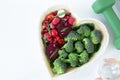 Heart-shaped plate with plant-based healthy food, green dumbbell, and hand holding a glass of water on white, top view Royalty Free Stock Photo