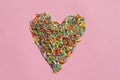 Heart shaped rainbow sugar sprinkle dots, decoration for cake and bakery on colored backdrop. Colorful sprinkles on pink