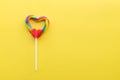 Heart shaped rainbow swirl lollipop on bright yellow solid background