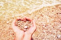 Heart shaped sea pebbles in female hands on the background of the sea beach and waves on a summer sunny day.