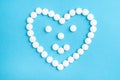Heart shaped smile made from white medical pills on blue paper background