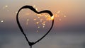 Heart-shaped sparkler burning against background of sea at dawn