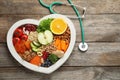 Heart shaped tray with healthy products and stethoscope on wooden background, top view. Royalty Free Stock Photo