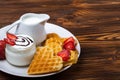 Heart shaped waffles with strawberries, cream sauce, pitcher with milk on white plate and black background. Royalty Free Stock Photo