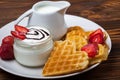 Heart shaped waffles with strawberries, cream sauce, pitcher with milk on white plate and wood background. Royalty Free Stock Photo