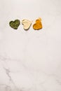 Heart shapes of dried basil, ginger and turmeric powder spices on marble background